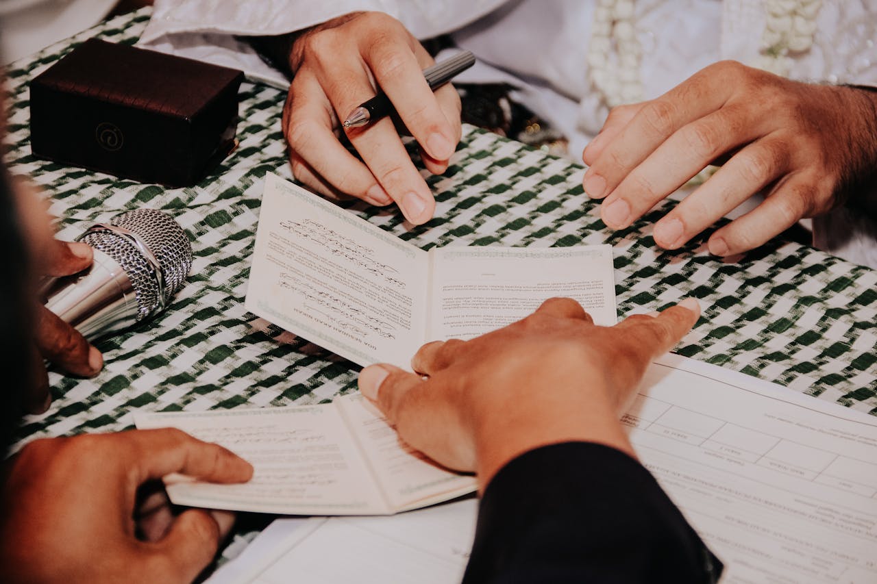 Multiple hands holding and signing a document during a formal ceremony with a microphone nearby.